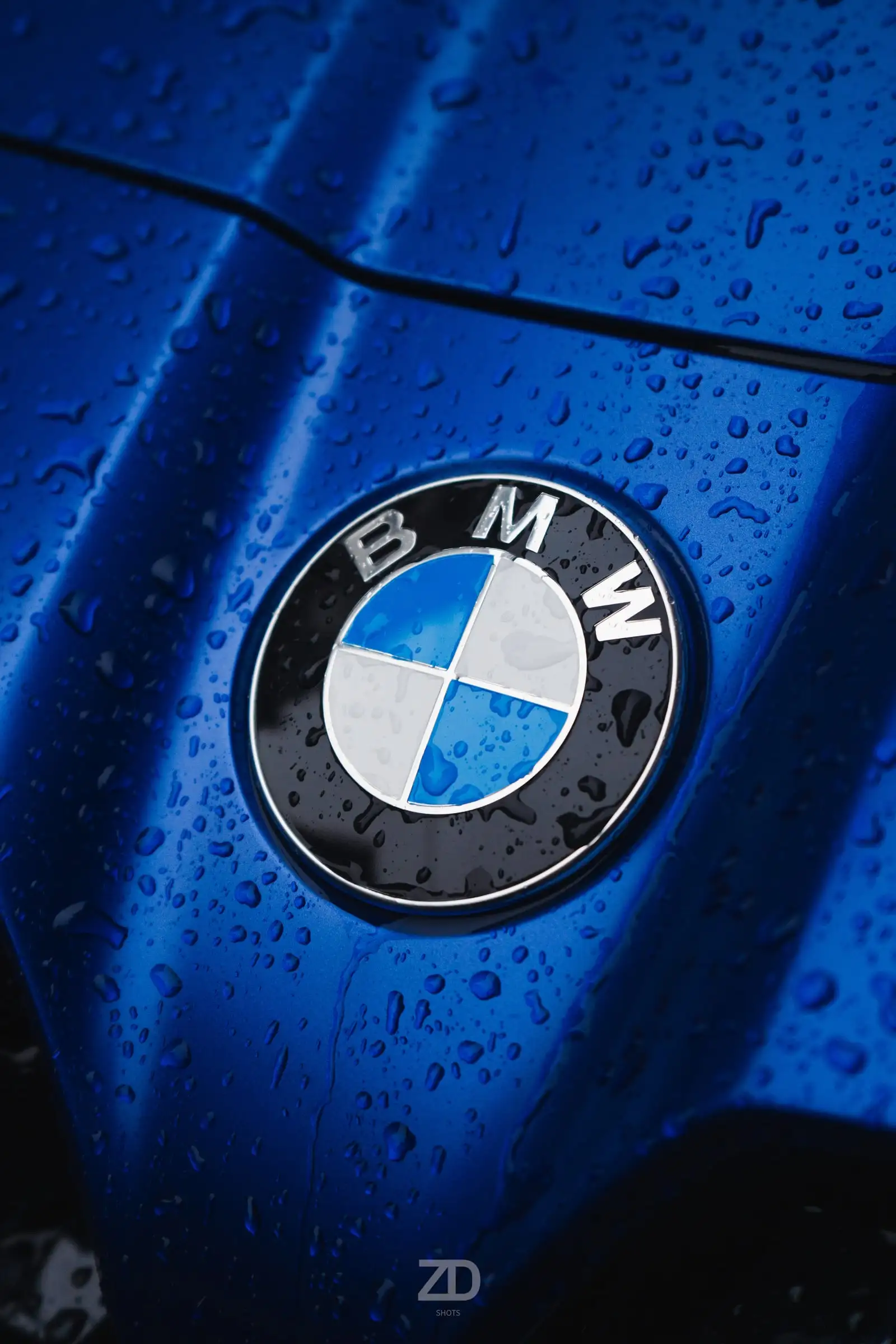 Markenemblem auf blauem Lack mit Regentropfen