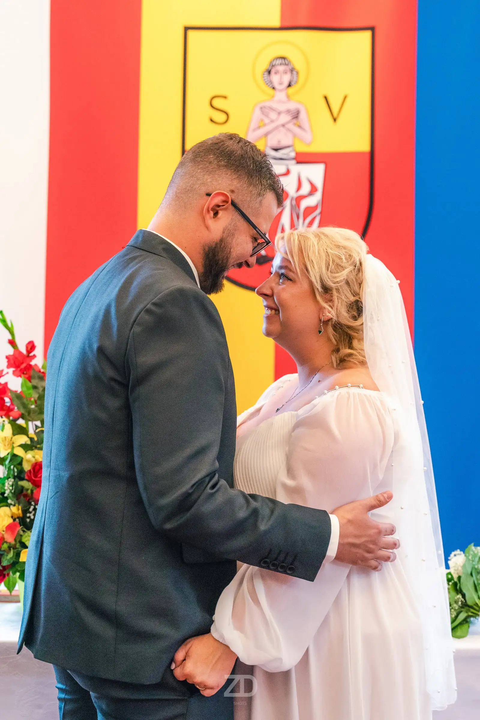 Brautpaar umarmt sich vor einer bunten Wappenwand