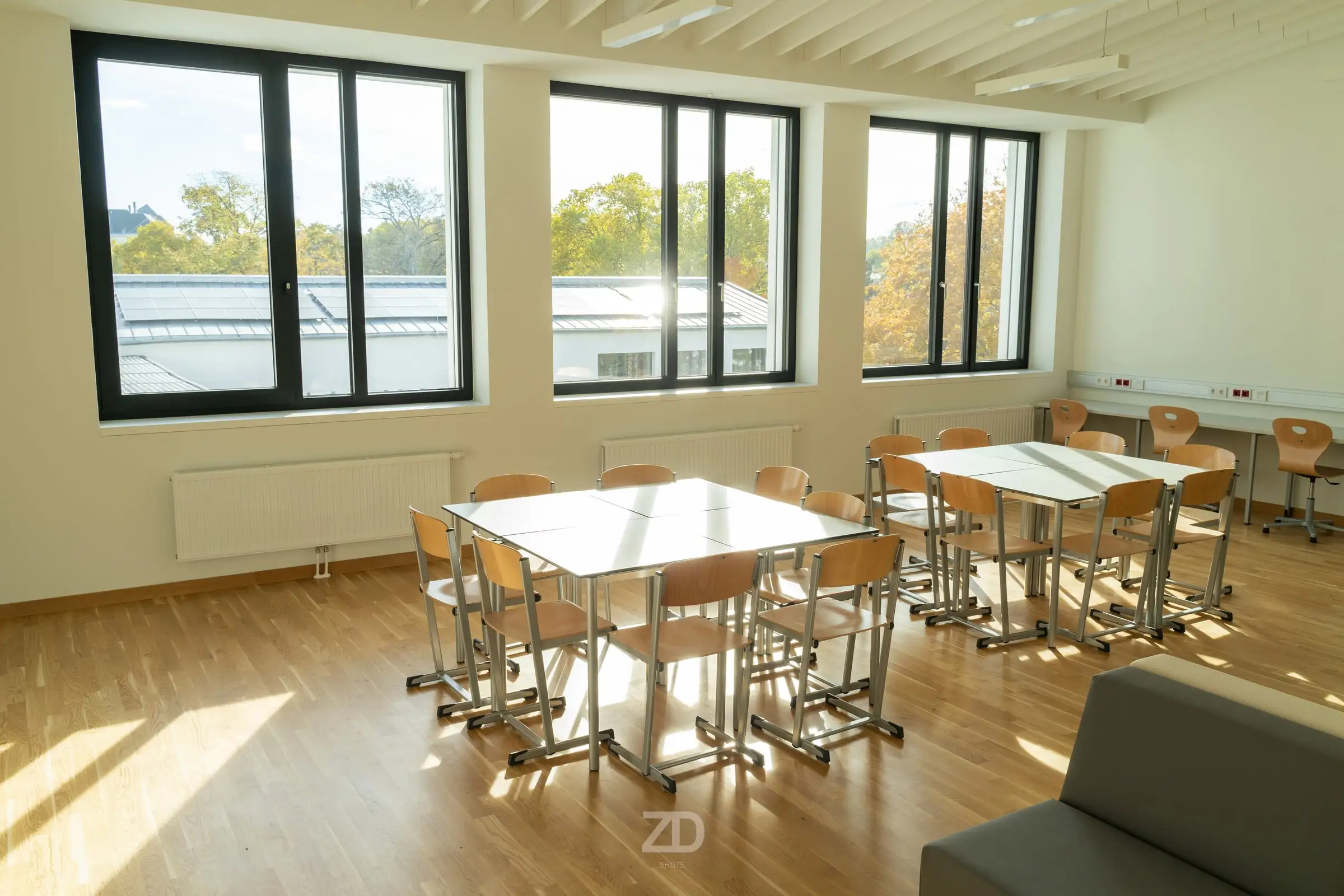 Sonniges Klassenzimmer mit Tischgruppen und großen Fenstern