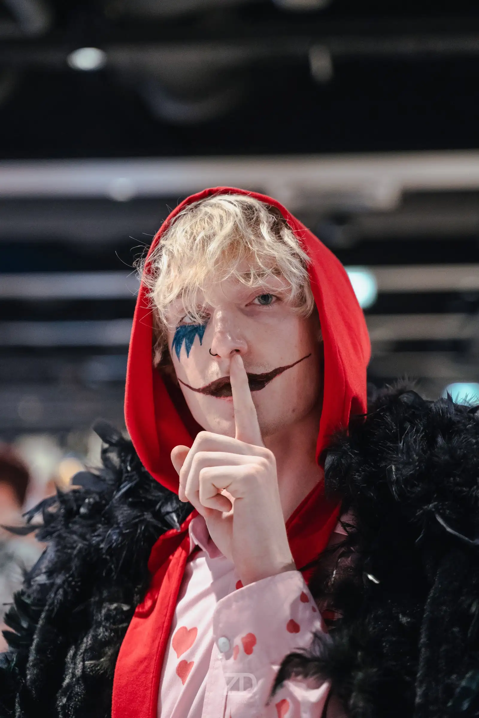 Cosplayer mit rotem Umhang hält den Finger an die Lippen