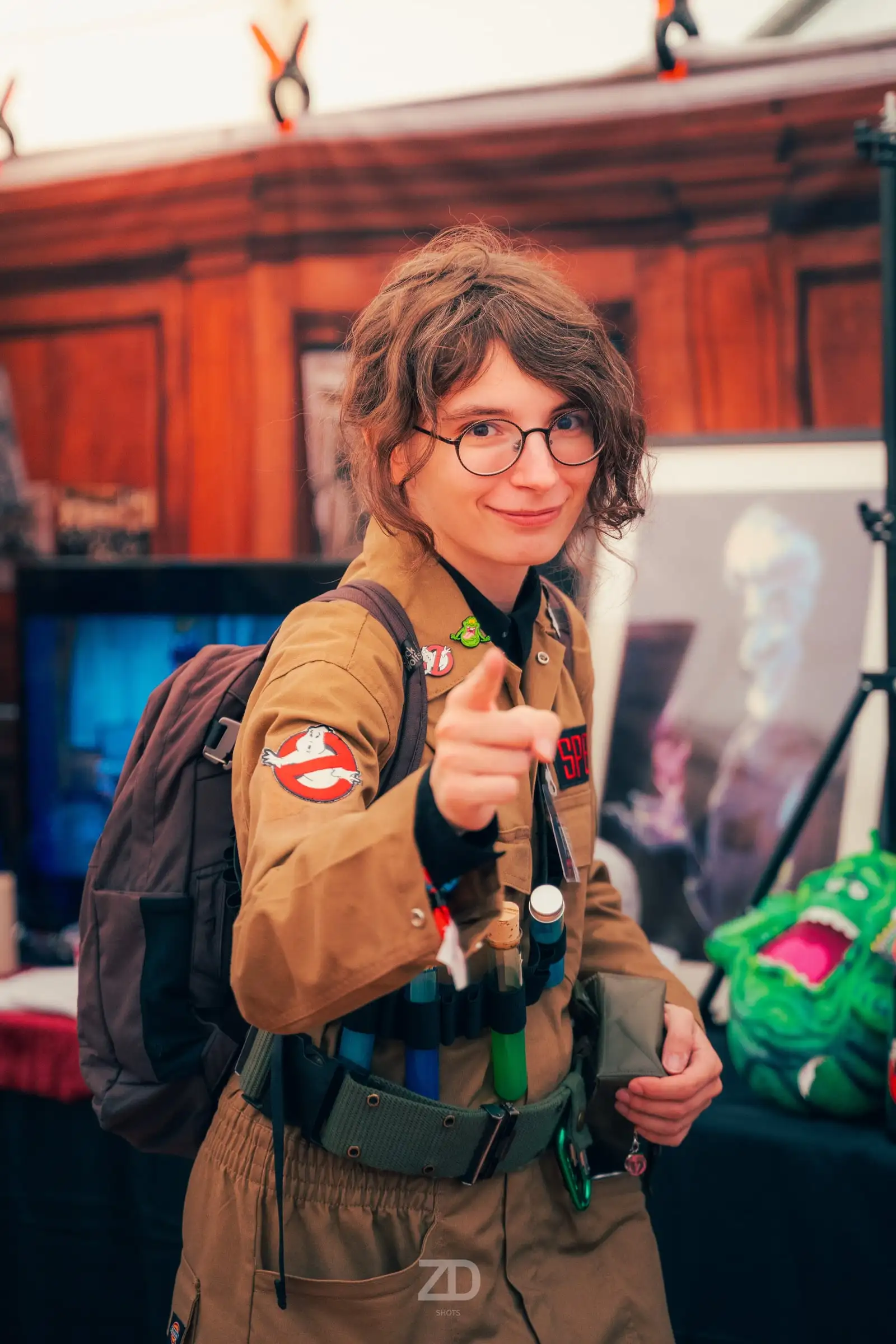 Cosplayerin in beiger Uniform zeigt lachend auf die Kamera