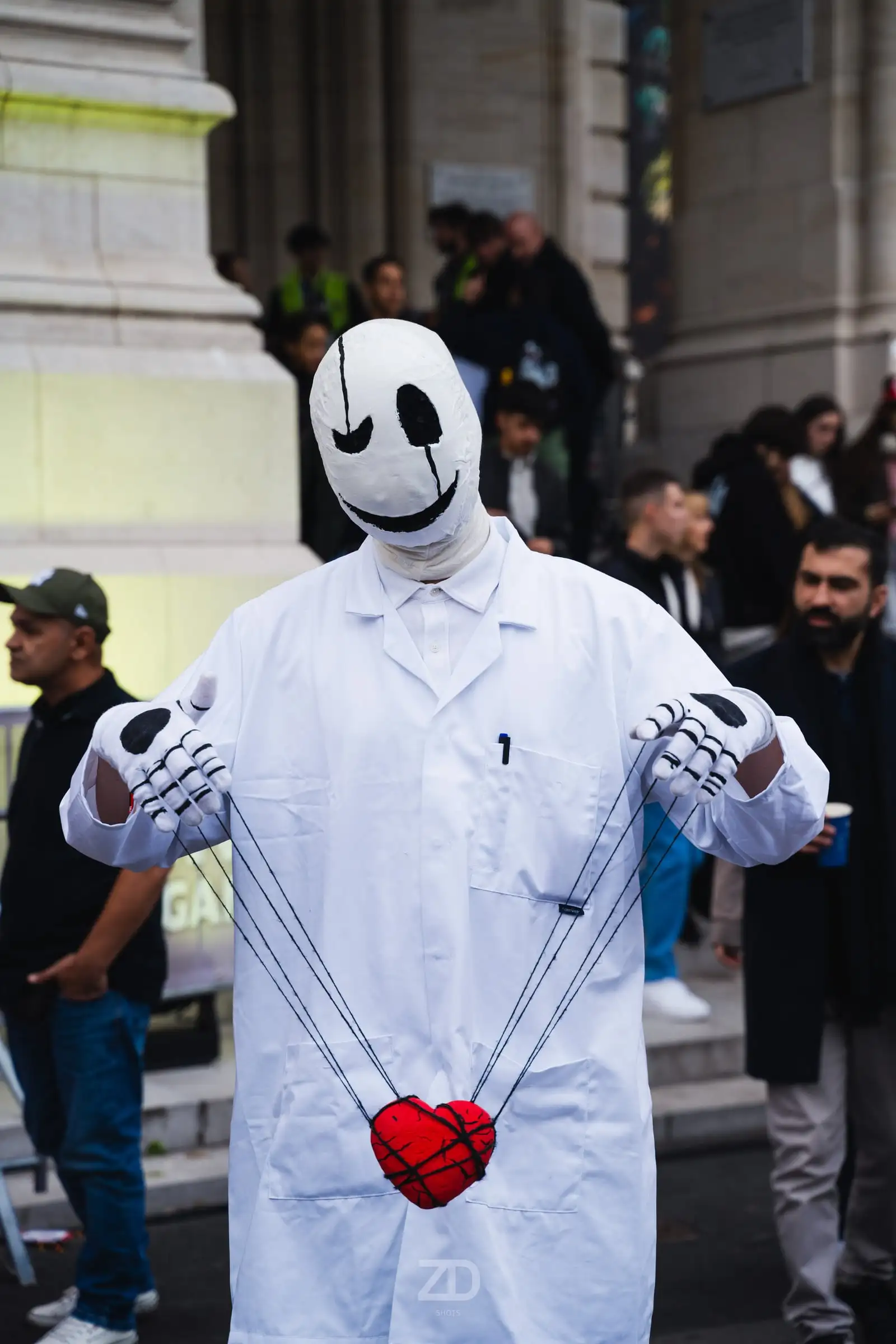 Cosplayer in weißem Mantel mit Maske vor einer Säulenfassade