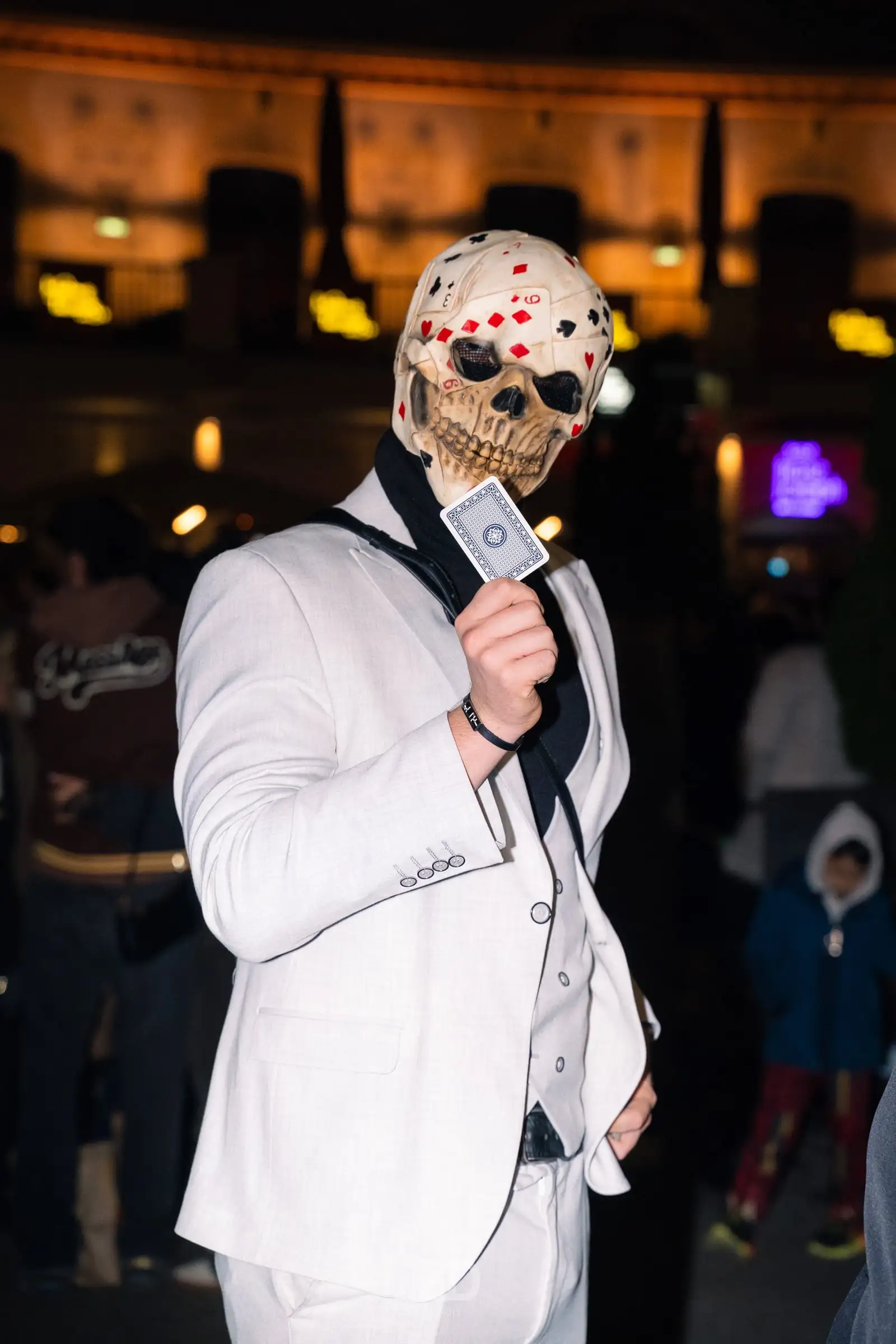 Person im weißen Anzug mit Maske hält eine Spielkarte