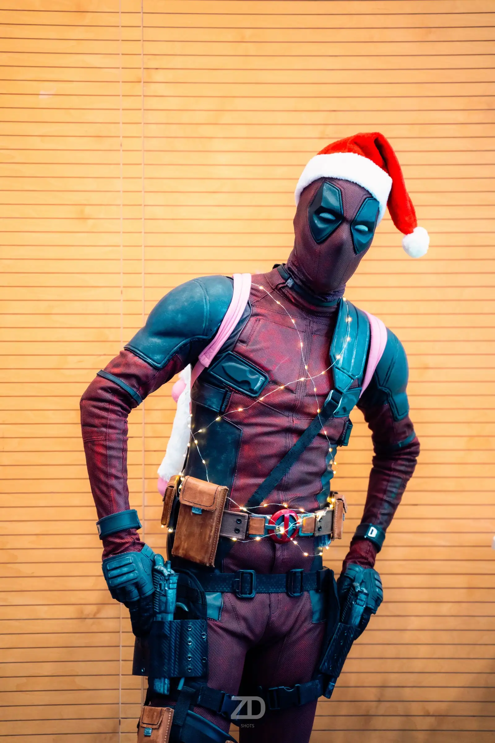 Cosplayer im rot-blauen Anzug mit Weihnachtsmütze vor Holzwand