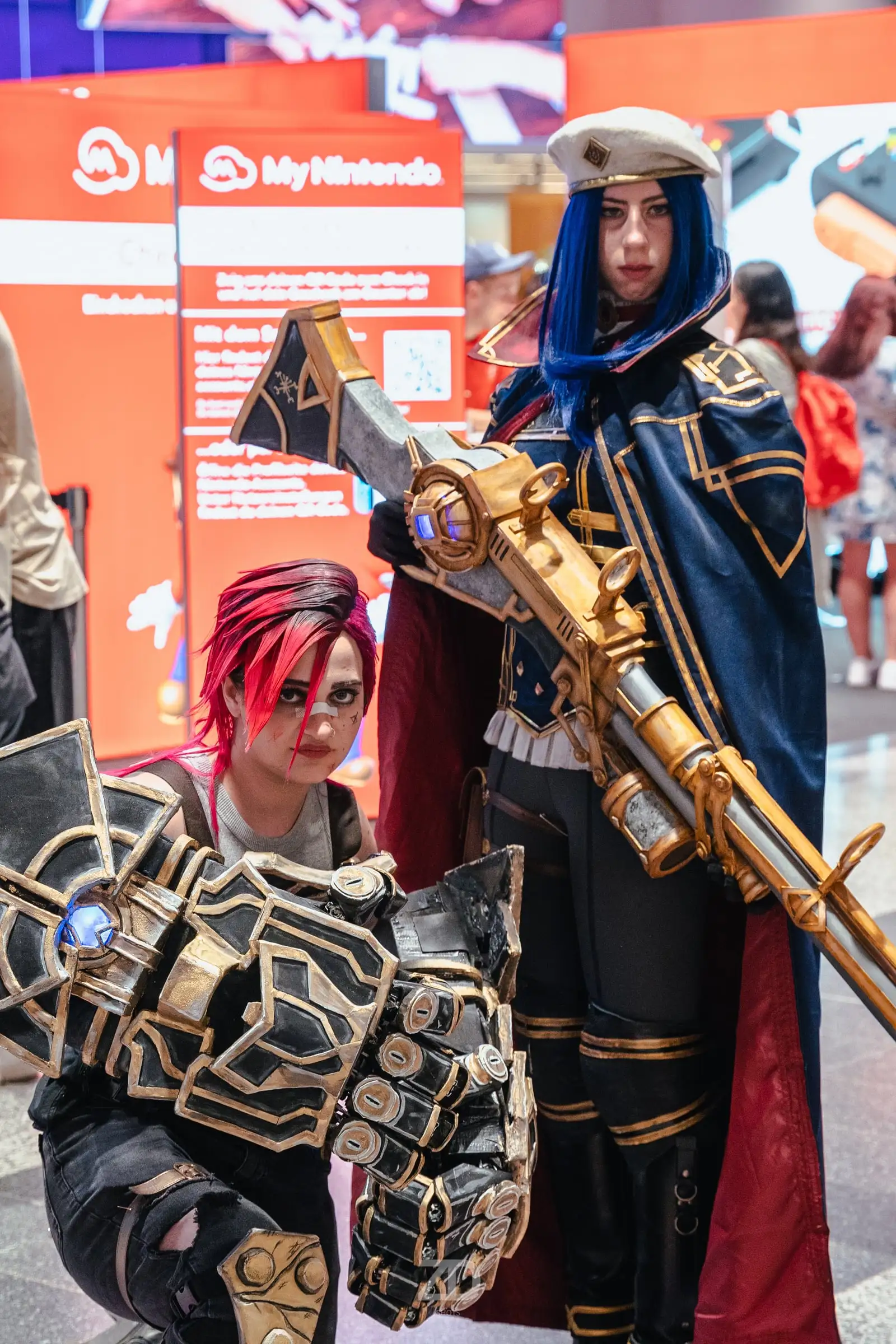 Zwei Cosplayerinnen mit riesigem Handschuh und goldenem Gewehr auf einer Messe