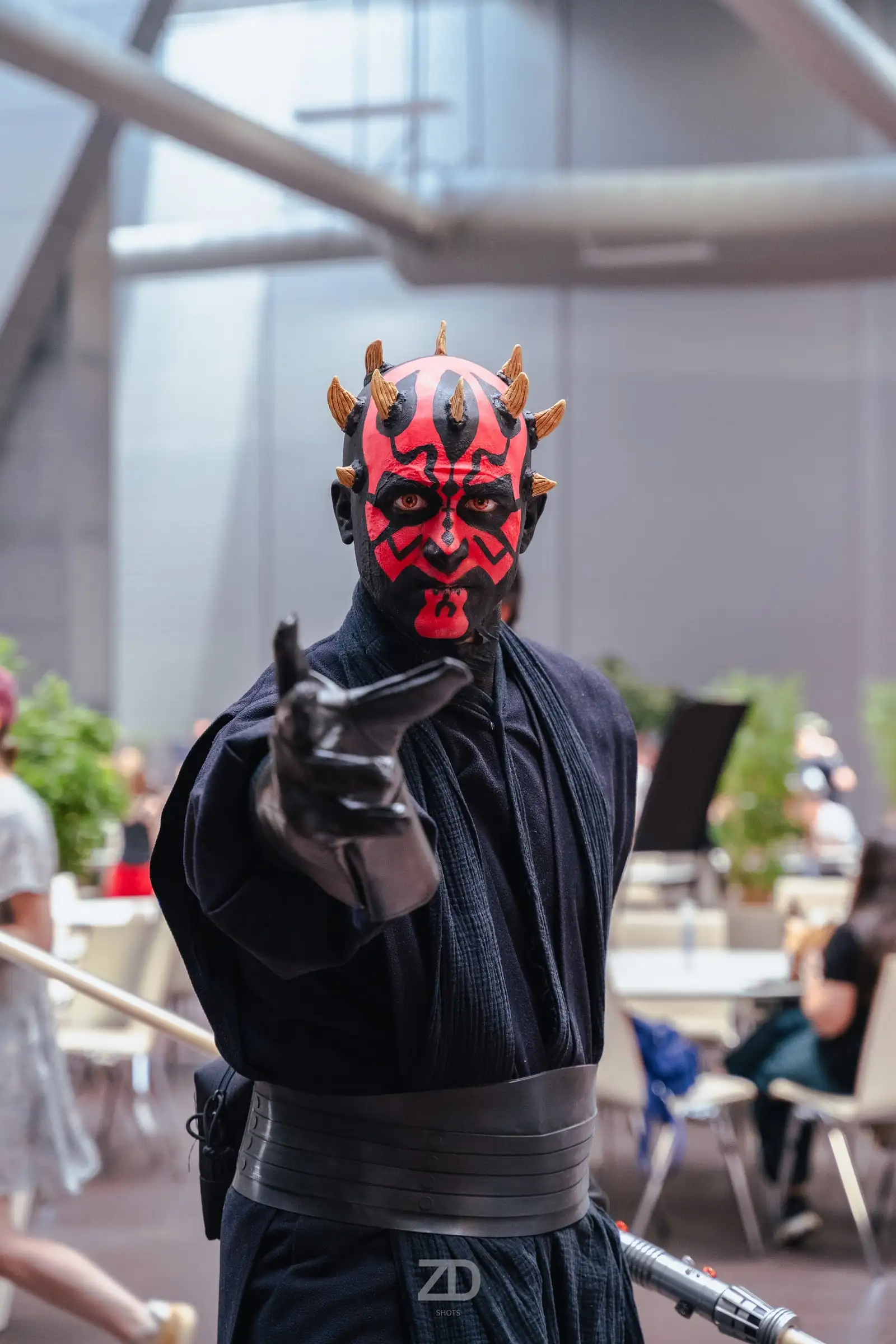 Cosplayer mit rot-schwarzer Gesichtsbemalung zeigt auf die Kamera
