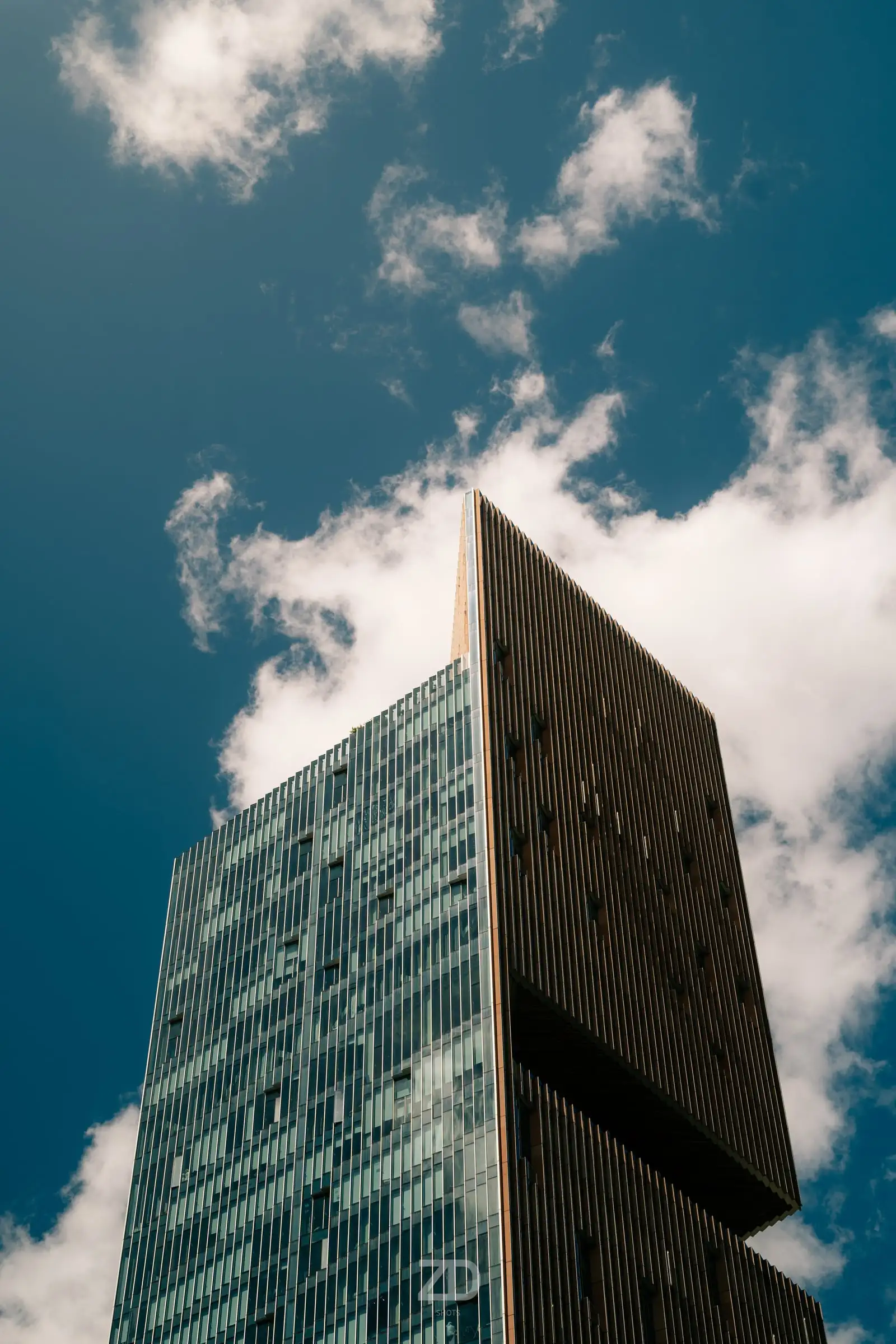 Dunkles Hochhaus vor blauem Himmel mit Wolken