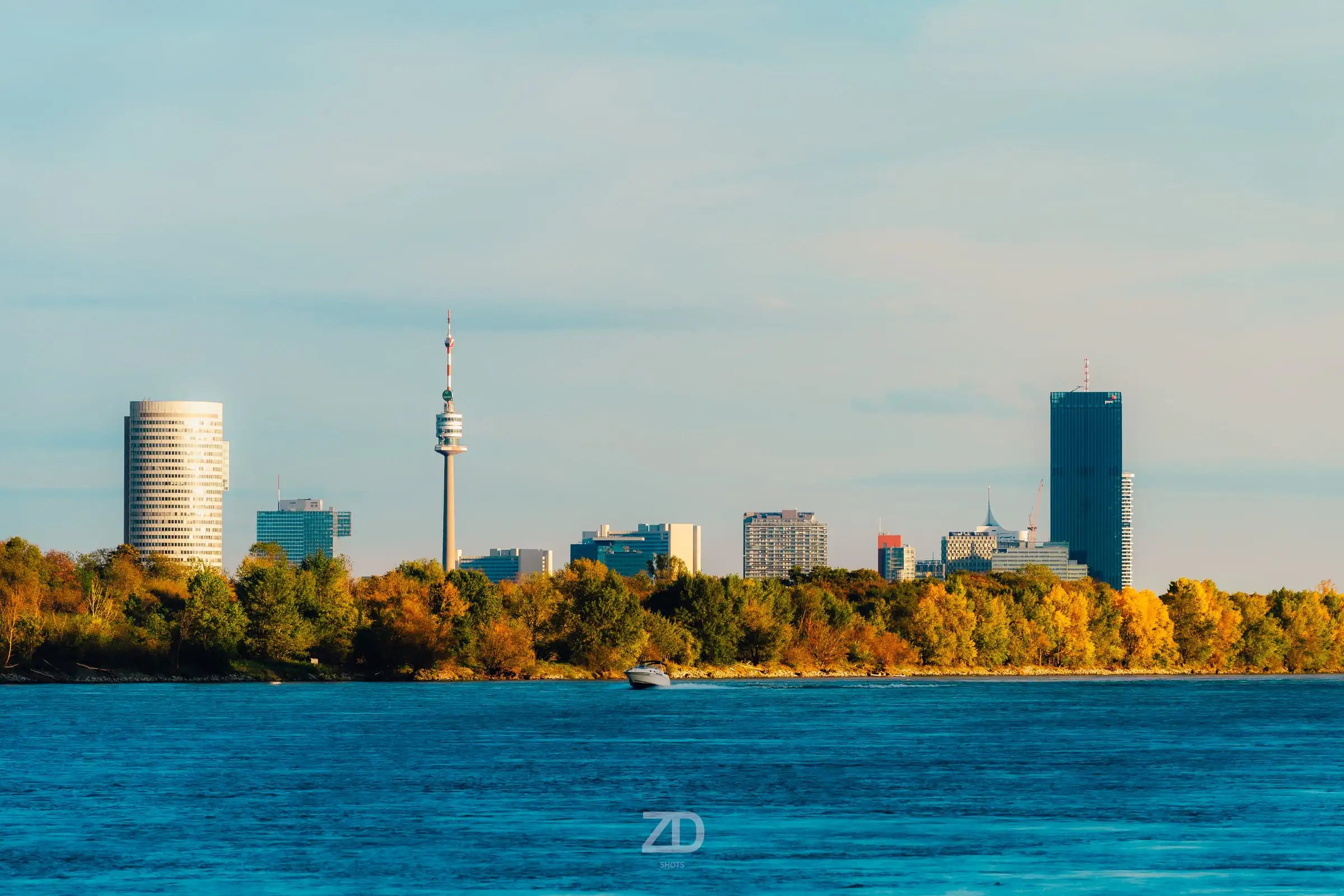 Skyline mit Donauturm und Hochhäusern über dem Wasser, davor herbstliche Bäume