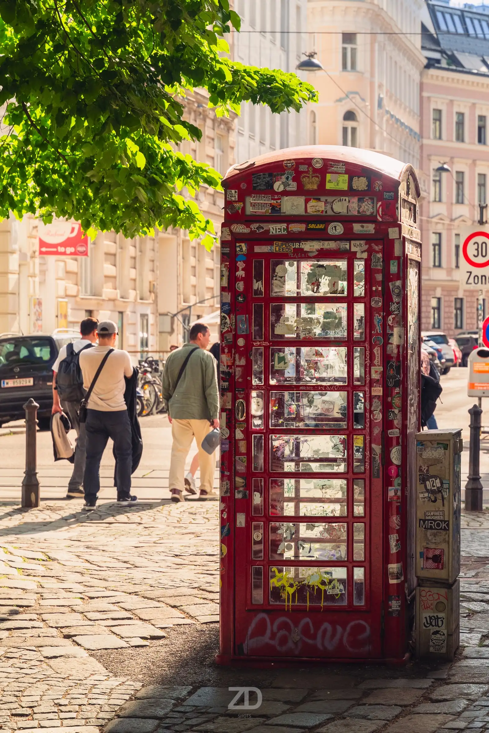 Rote Telefonzelle voller Aufkleber in einer Altbaugasse