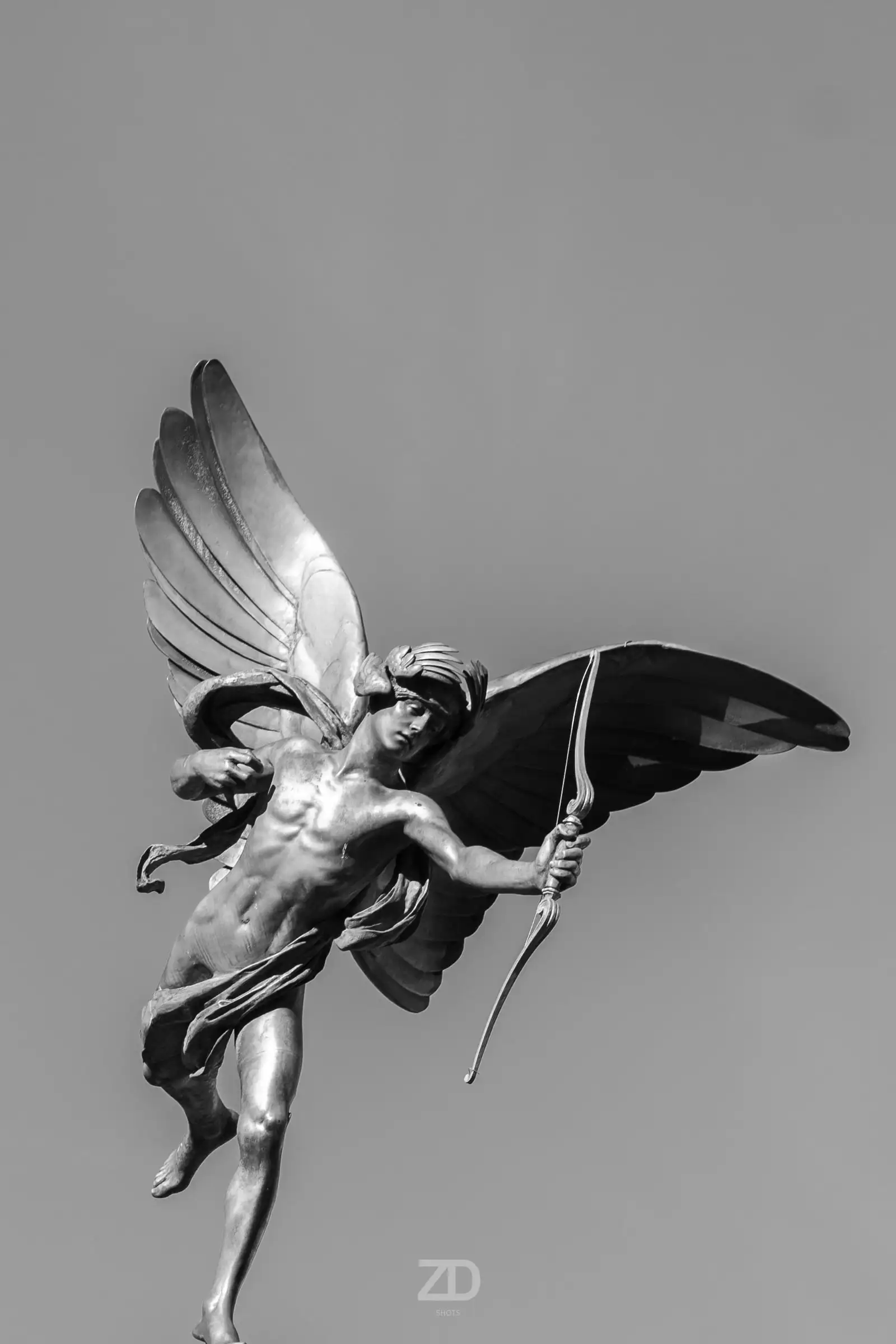 Bronzefigur mit Flügeln vor hellem Himmel